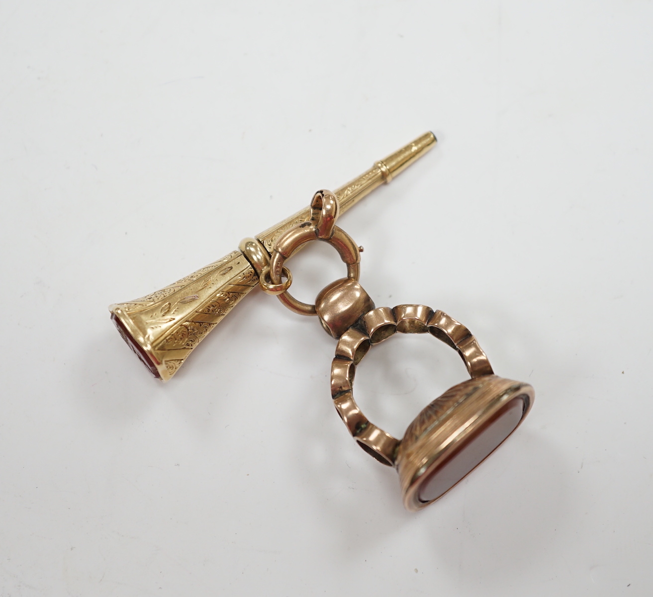 A 19th century engraved yellow metal overlaid and carnelian set trumpet shaped watch key, the matrix carved with crest and initial, 51mm, together with a 19th century gold plated and carnelian set fob.